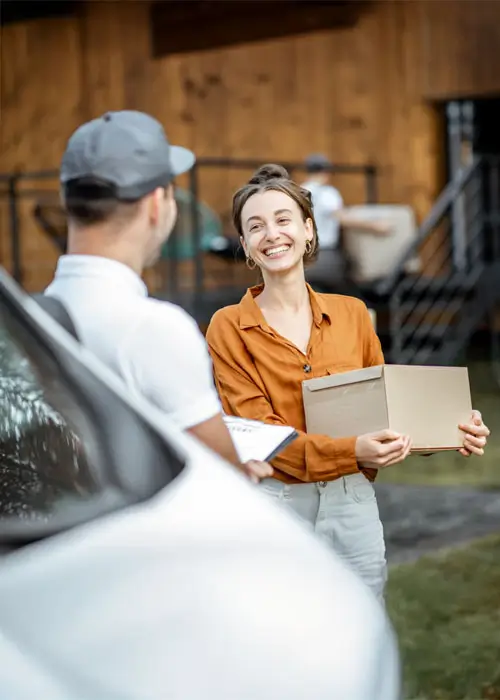 Portrait of a happy client with a male courier delivering goods by vehicle to a woman home, workman moving parcels on the background.