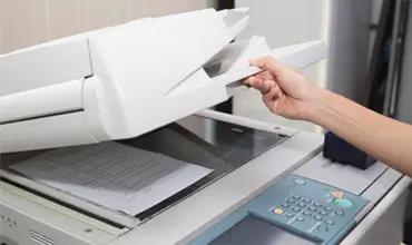 woman hands putting a sheet of paper into a copying device or printer in the office.